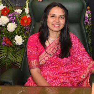 Senior woman advocate seated in a chair wearing a pink saree with a floral backdrop at MP Legal Consultants.